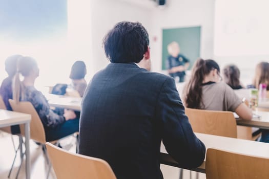 Teacher at university in front of a whiteboard screen. Students listening to lecture and making notes