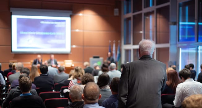 I have a question. Group of business people sitting at the chairs in conference hall. Businessman raising his arm. Conference and Presentation. Business and Entrepreneurship.