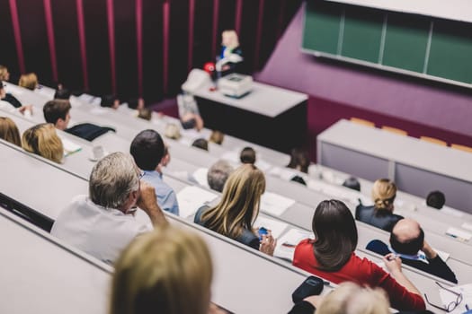 Lecturer at university. Healthcare expert giving a talk to medical faculty professors. Participants listening to lecture and making notes.