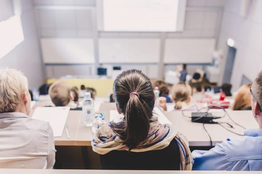Students listening to lecture and making notes. Professor giving presentation in lecture hall at university.