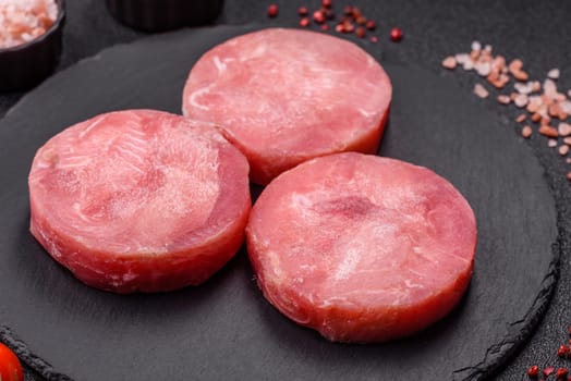 Two fresh slices of raw tuna fillet with spices and herbs on a dark concrete background