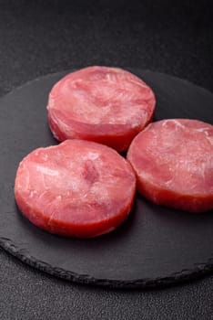 Two fresh slices of raw tuna fillet with spices and herbs on a dark concrete background