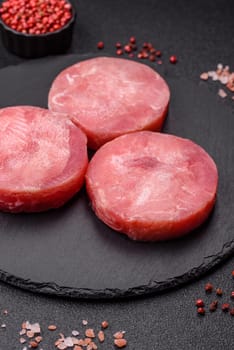 Two fresh slices of raw tuna fillet with spices and herbs on a dark concrete background
