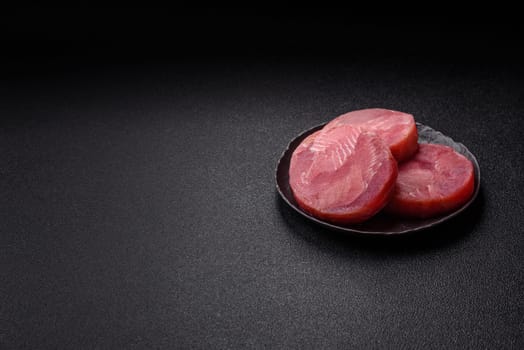 Two fresh slices of raw tuna fillet with spices and herbs on a dark concrete background