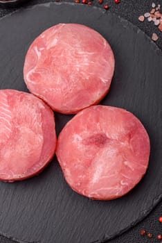 Two fresh slices of raw tuna fillet with spices and herbs on a dark concrete background