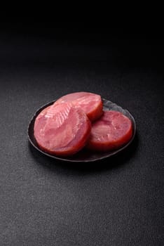 Two fresh slices of raw tuna fillet with spices and herbs on a dark concrete background