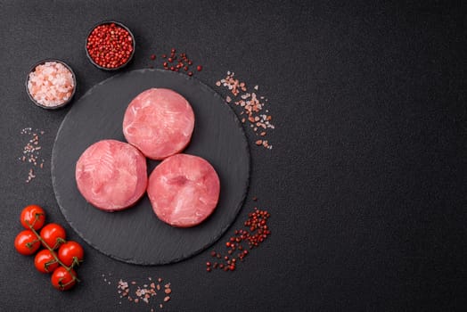 Two fresh slices of raw tuna fillet with spices and herbs on a dark concrete background