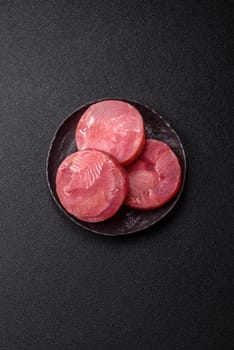 Two fresh slices of raw tuna fillet with spices and herbs on a dark concrete background