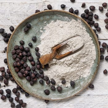 Plate and wooden scoop of black chickpea flour and beans top viewon white wooden table. Traditional beans from Apulia and Basilicata in Italy