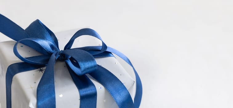 Grey Wrapped Christmas present with a blue ribbon bow on grey close up with copy space. Grey and blue winter composition with Gift box, copy space