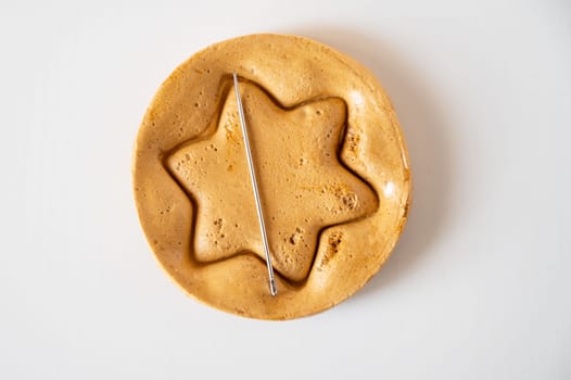 Brown sugar caramel candy cookies with a metal needle in the shape of a star on a white background.