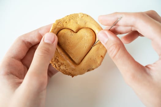 Hands closeup scratch brown sugar caramel candy cookies with a metal needle in the shape of a heart on a white backgound