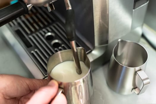 A man's hands beat milk for cappuccino.