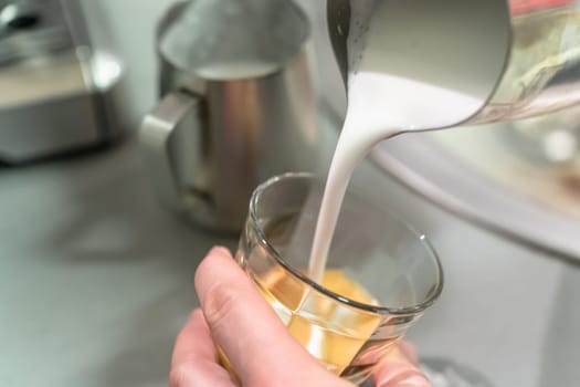 Barista pours milk foam into an espresso glass.