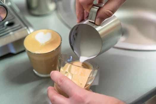 Barista prepares cappuccino, pours whipped milk into a glass of espresso.