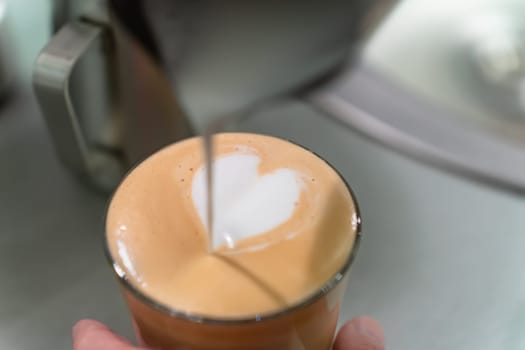 Barista made a drawing with milk in the shape of a heart in a glass with cappuccino.