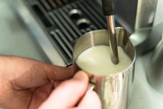 A man foams milk for a cappuccino in a pitcher.