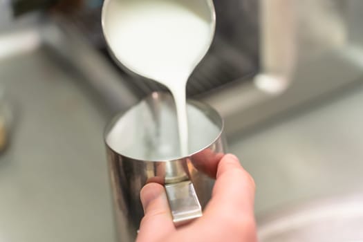 A barista pours whipped milk from one steel jug into another.