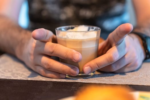 Selective focus on the hands of a man holding a glass of cappuccino, spreading his index fingers
