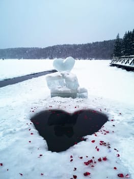 Heart-shaped hole on an ice-covered winter lake with rose petals.