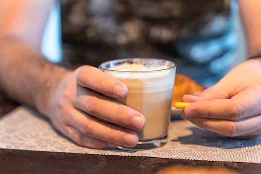 Selective focus on a man's hands, a glass of coffee in one hand and a capsule of medication in the other