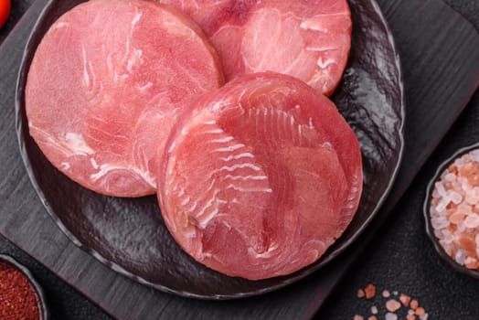 Two fresh slices of raw tuna fillet with spices and herbs on a dark concrete background