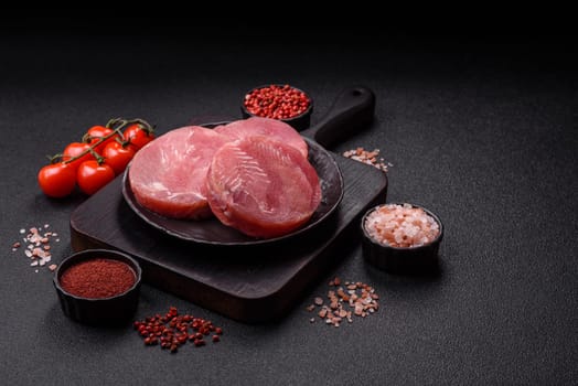 Two fresh slices of raw tuna fillet with spices and herbs on a dark concrete background