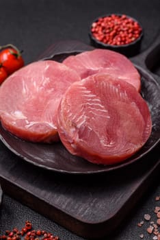 Two fresh slices of raw tuna fillet with spices and herbs on a dark concrete background