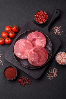 Two fresh slices of raw tuna fillet with spices and herbs on a dark concrete background