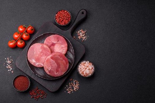 Two fresh slices of raw tuna fillet with spices and herbs on a dark concrete background