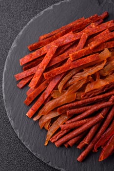 Jerky, dried fish in the form of sticks with salt, spices and herbs on a dark concrete background