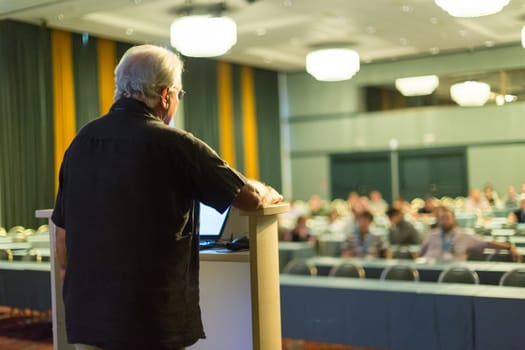 Casualy dressed senior professor giving talk at scientific conference. Audience at the conference hall. Research experts and entrepreneurship event.