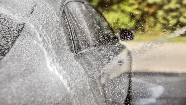 Abstract carwash background - only drops in focus. Car being washed at self service station, shampoo spraying.