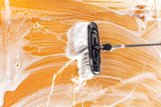 Brush leaving strokes in soap and foam on yellow car washed in carwash.