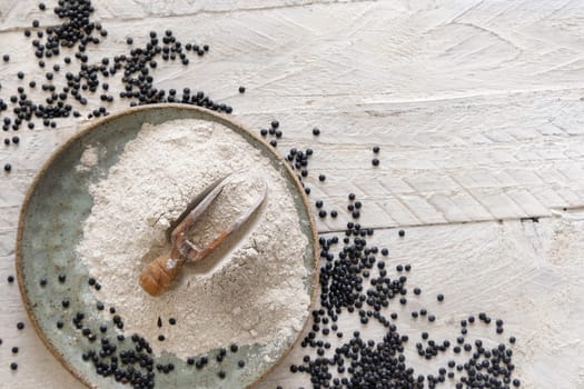 Plate with a scoop of black lentils flour and beans on white wooden table top view with copy space. Alternative flour, healthy eating, vegetarian concept. Traditional Asian and North African cuisines