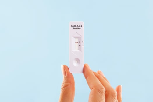 Woman holding COVID-19 coronavirus antigen rapid test over blue background. Selftesting at home.