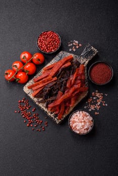 Jerky, dried fish in the form of sticks with salt, spices and herbs on a dark concrete background