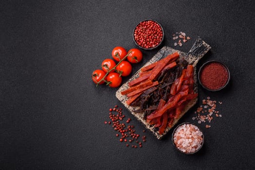 Jerky, dried fish in the form of sticks with salt, spices and herbs on a dark concrete background