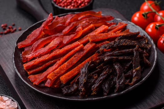 Jerky, dried fish in the form of sticks with salt, spices and herbs on a dark concrete background