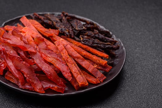 Jerky, dried fish in the form of sticks with salt, spices and herbs on a dark concrete background