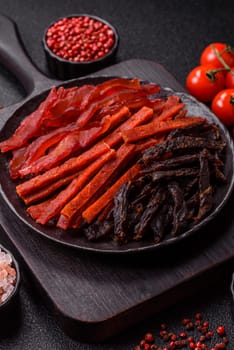 Jerky, dried fish in the form of sticks with salt, spices and herbs on a dark concrete background