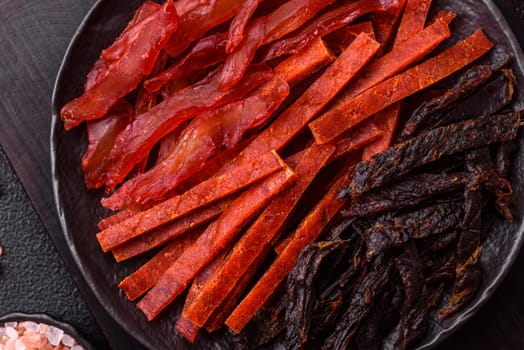 Jerky, dried fish in the form of sticks with salt, spices and herbs on a dark concrete background