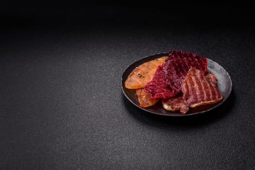 Jerky, dried meat in the form of slices with salt, spices and herbs on a dark concrete background