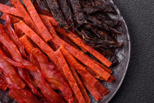 Jerky, dried fish in the form of sticks with salt, spices and herbs on a dark concrete background