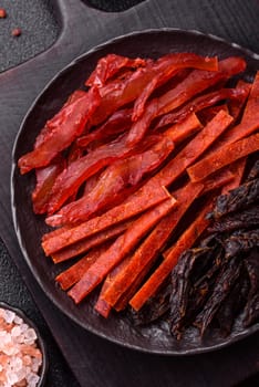 Jerky, dried fish in the form of sticks with salt, spices and herbs on a dark concrete background