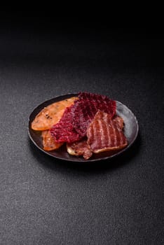 Jerky, dried meat in the form of slices with salt, spices and herbs on a dark concrete background