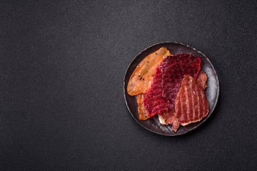 Jerky, dried meat in the form of slices with salt, spices and herbs on a dark concrete background