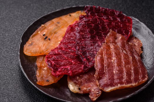 Jerky, dried meat in the form of slices with salt, spices and herbs on a dark concrete background