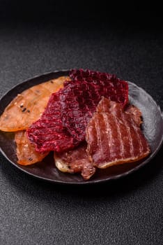 Jerky, dried meat in the form of slices with salt, spices and herbs on a dark concrete background