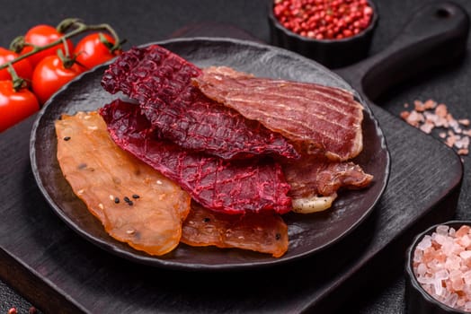 Jerky, dried meat in the form of slices with salt, spices and herbs on a dark concrete background